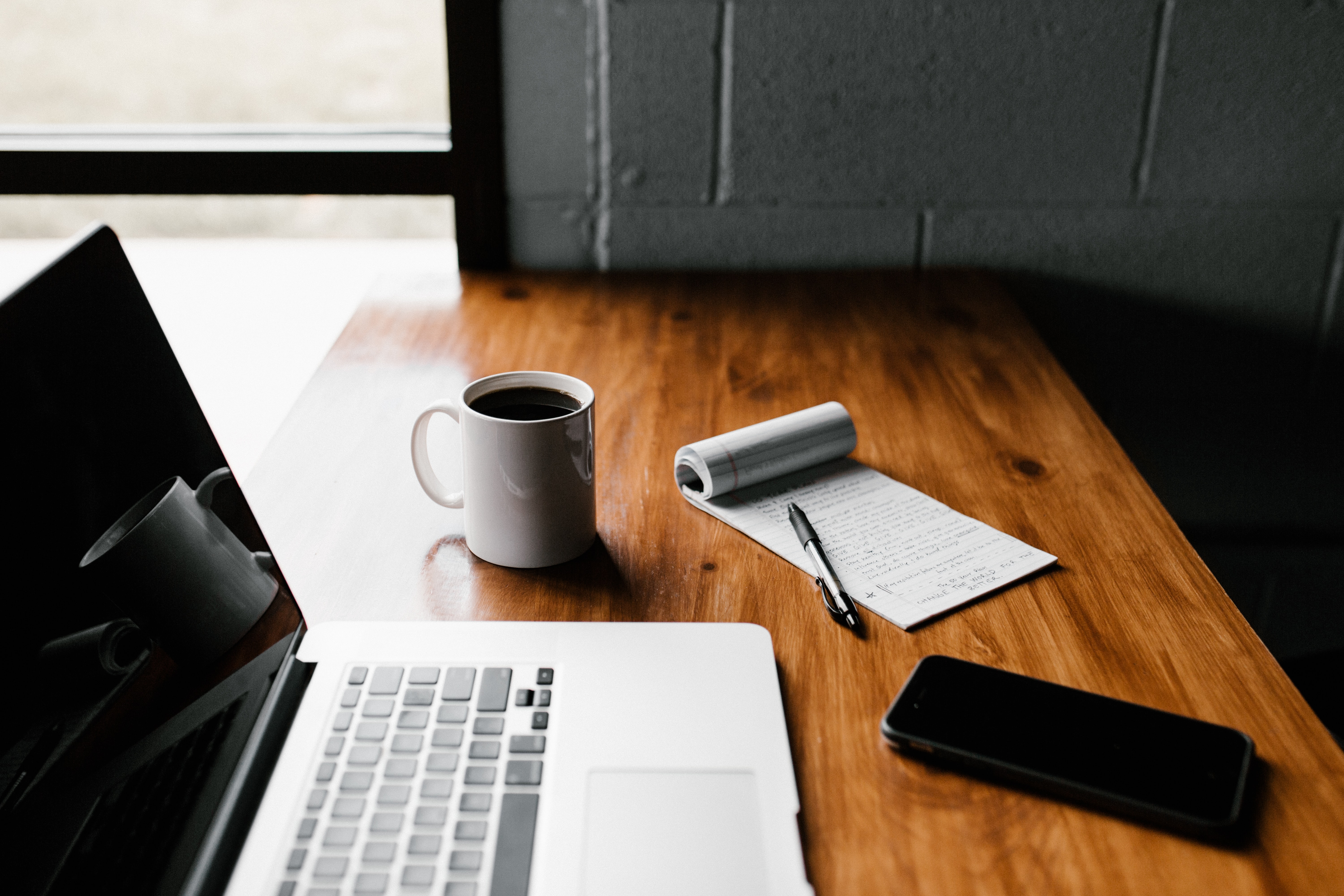 photograph of an opened macbook, notebook, and coffee on a glossed oak wood table